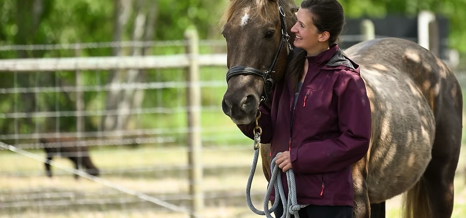 woman walking with horse, holding lead rope and petting horse's face.